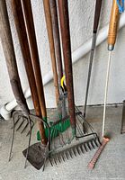 Group of long-handled garden tools showing heads: fork, spade, rakes, rod, wire brush