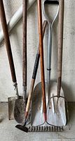 All five long-handled garden tools leaning against wall