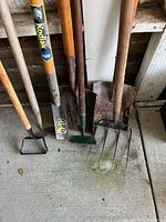 Close view of tool heads: stirrup hoe, Kodiak shovel, narrow spade, rusted spade, pitchfork