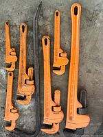 Group of six orange pipe wrenches with steel pry bar