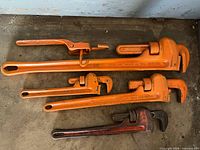 Five pipe wrenches laid out showing full length and color