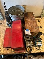 Overview showing bucket, wooden and red toolboxes, Makita chargers, drill bits