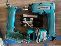 Two teal Makita cordless drills, five black stick batteries, one charger