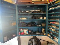 Full view of open blue cabinet showing assorted tapes, spray cans, hardware and side‐door bins of fasteners