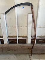 Full view of scythe showing wooden snath and curved blade
