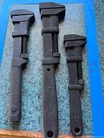 Three vintage adjustable monkey wrenches laid out side by side showing sizes and condition