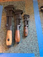 Front view of three vintage wood-handle adjustable monkey wrenches, showing size differences and screw mechanisms