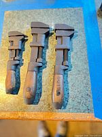 Three vintage adjustable monkey wrenches laid out to show size difference, metal bodies and wooden handles