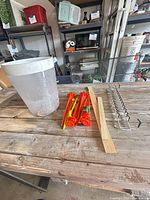 All items on table: plastic bucket, stakes, wood stick, metal rack