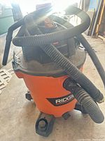 Ridgid orange/black canister vacuum with hose attached on casters