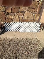 Stacked white vinyl lattice panels against stone wall