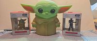 Grogu coin bank flanked by two boxed Hallmark Star Wars ornaments