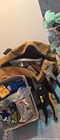 Overall view of canvas tool bag with tools visible including aviation snips, pliers, tape roll and outlet adapter