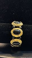 Front view of gold tone bracelet showing black cabochon stones and textured frames