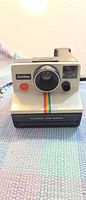 Front view of Polaroid OneStep Land Camera showing lens, shutter button, rainbow stripe