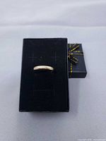 Gold band ring resting on black ring box