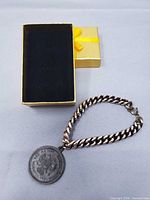Bracelet laid beside open gold box, full view of chain and medallion