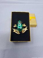 Front view of gold tone green enamel frog brooch in box