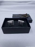 Pair of cufflinks in black box showing square faces and linear design
