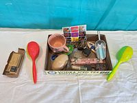Overview of lot showing mug, spoons, scoop, wooden egg, keychain, spring, dish, matchbox and other items in cardboard tray
