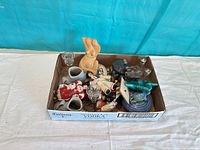 Boxed assortment of trinkets showing ceramic torso, bud vases, glass votives, lidded box, dishes, ornaments and thimbles