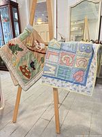 Front view of both baby quilts on easel, showing designs and colors