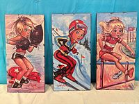 Front view of three Jolylle plaques showing artwork and signatures