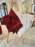 Red and black floral blanket alongside white textured blanket displayed on stand