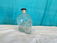 Front view of clear glass skull bottle with cap