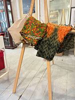 Three fabric lengths draped on easel: beige solid, multicolour leaf print, green-orange patterned