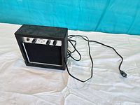 Front view of First Act mini amplifier showing control panel, grille and attached power cord