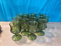 Front angled view of all 14 green pressed glass goblets grouped together