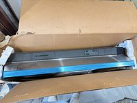 Range hood inside open box showing stainless steel body and control panel