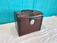 Closed brown crocodile-pattern leather jewelry box showing exterior, handle, latch