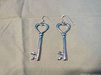 Front view of both silver key earrings on fabric background