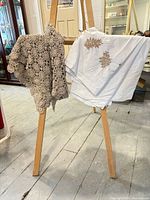 Beige crochet lace and white embroidered tablecloth draped on easel