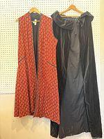 Front view of red brocade vest and black velvet cape on hangers