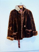 Front view of brown fur coat with beige fur collar, button, pockets, belt piece visible