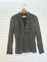 Long-sleeve ruffle-neck houndstooth blouse hanging on pegboard