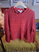 Front view of red openwork cotton sweater on hanger