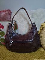 Front view of brown alligator-embossed leather shoulder bag showing exterior zip pocket and shape