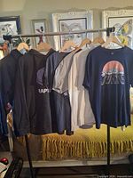 Seven garments on hanging rack showing variety of hoodies and tees