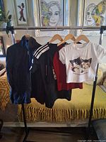 All four garments on rack: Adidas track jacket, navy jacket, red top, white kitten T-shirt