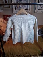 Front view of ivory cable-knit sweater on hanger