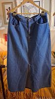 Front view of long blue denim skirt hanging on hanger
