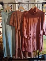 Three dresses hung on rack: teal sleeveless, rust puff-sleeve, rust cowl-neck
