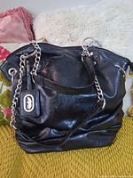 Front view of black faux leather Marc Ecko shoulder bag showing chain strap, logo tag and overall shape