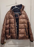 Front view of bronze Tommy Hilfiger hooded puffer jacket showing zipper, pockets, and logo