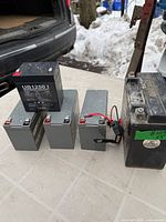 group shot of five sealed lead-acid batteries on table, snow and vehicle in background