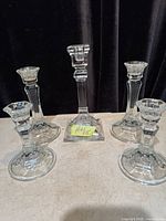 Five clear glass candlesticks displayed upright on surface